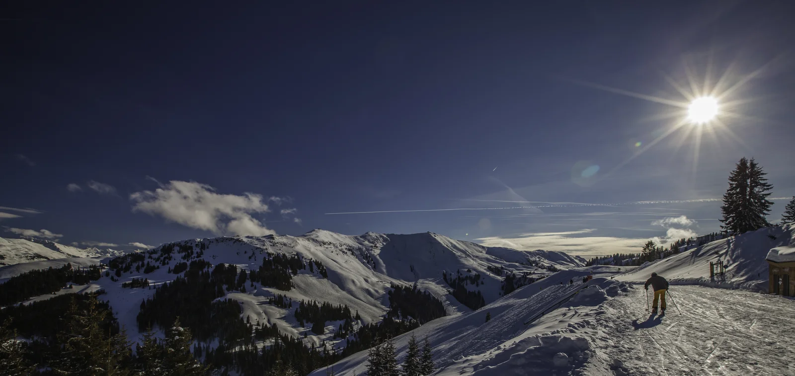 Panoramic view of snow-covered alpine peaks and groomed ski runs under a bright winter sky in Kitzbühel.