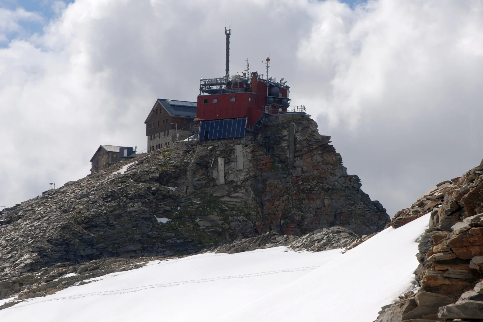 High mountain meteorological observatory perched on a rocky alpine summit surrounded by snow and ice.