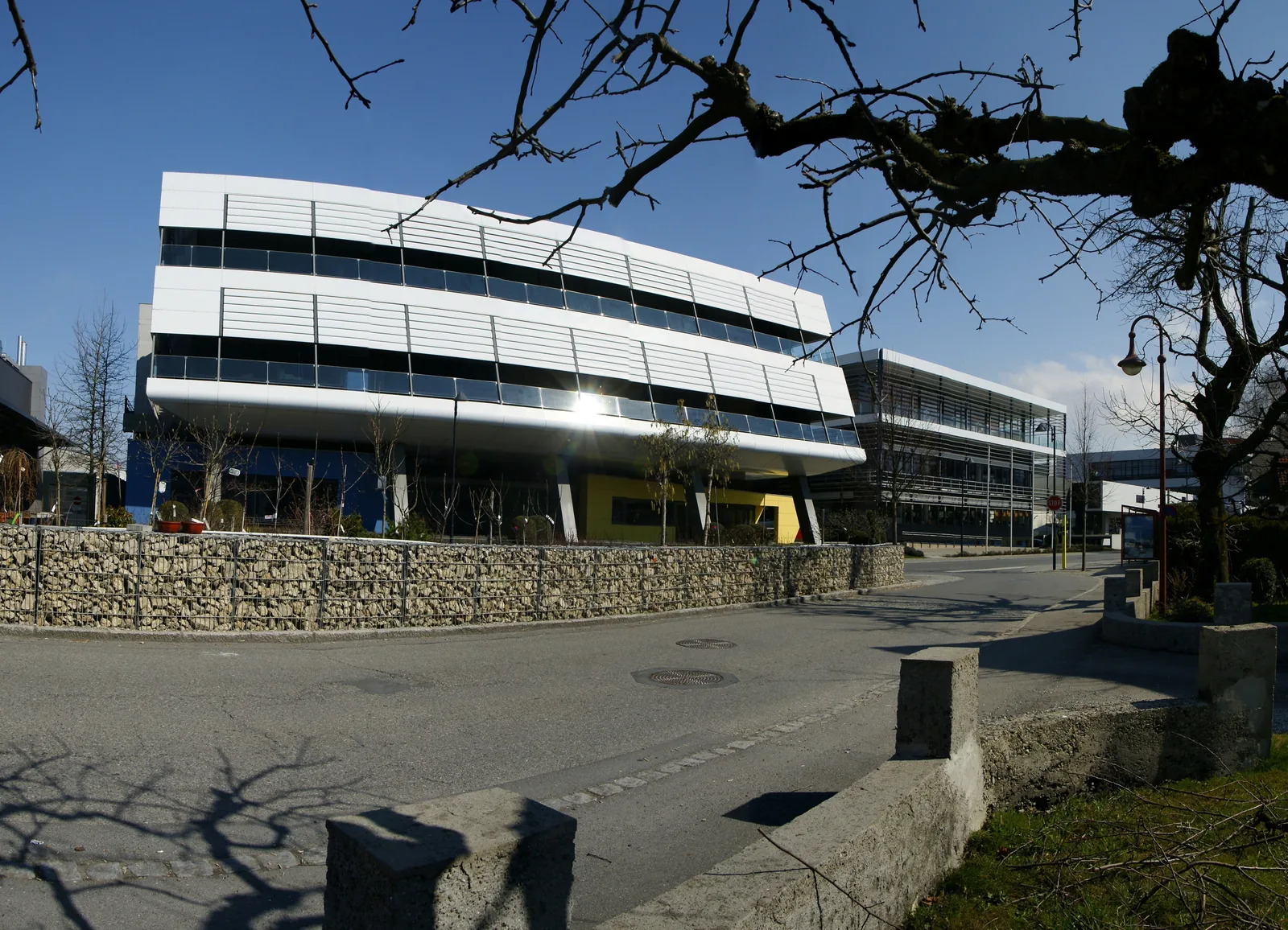 Modern multi-storey industrial factory complex and research facilities surrounded by green meadows in Höchst, Vorarlberg.