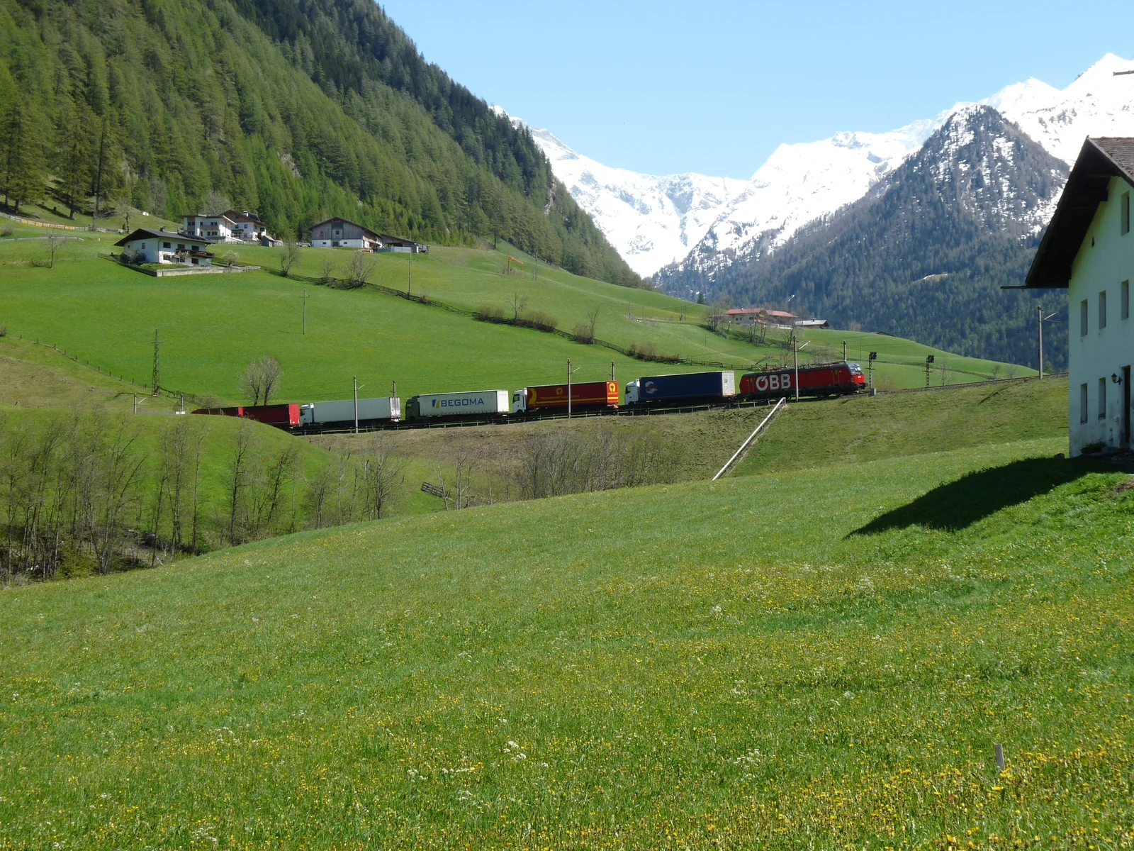 Electric railway locomotives and overhead catenary wires at an alpine border freight switching yard.