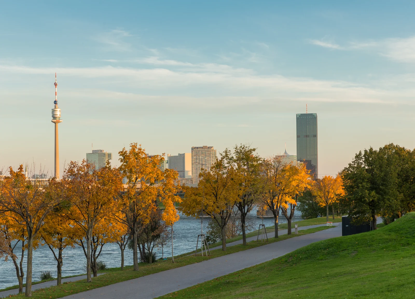 Panoramic view of the New Danube channel and grassy banks of Danube Island looking toward Vienna's modern skyline.
