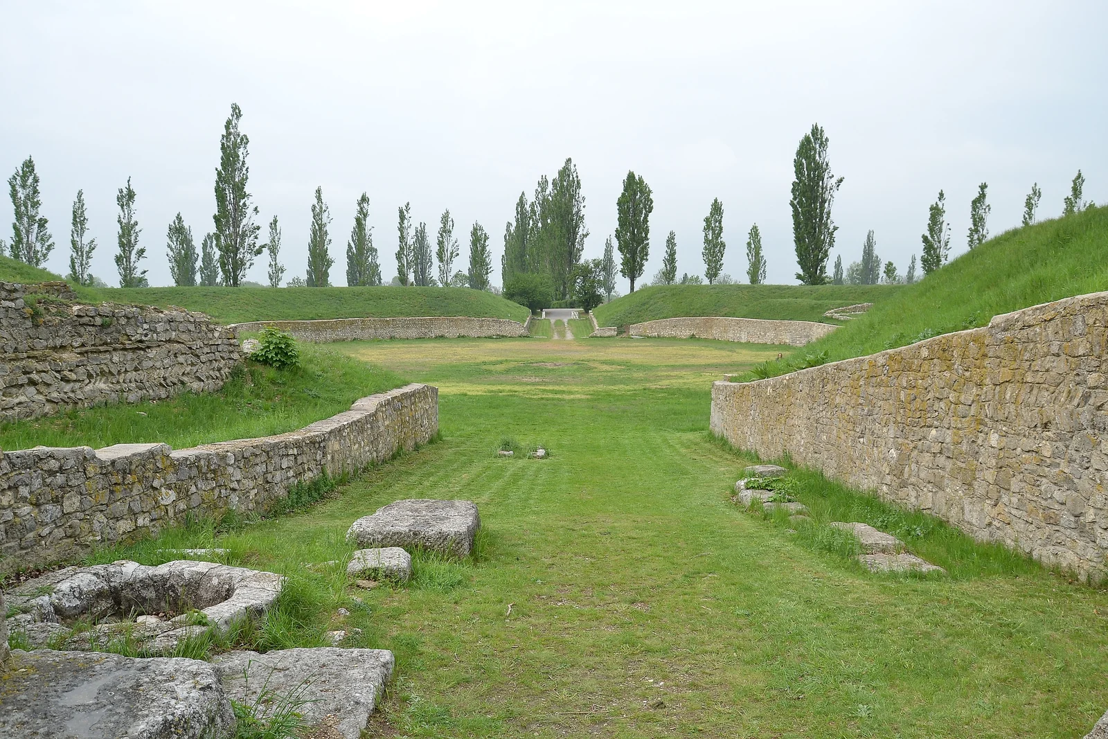 Excavated stone arena walls and grassy oval arena floor of an ancient Roman amphitheatre.
