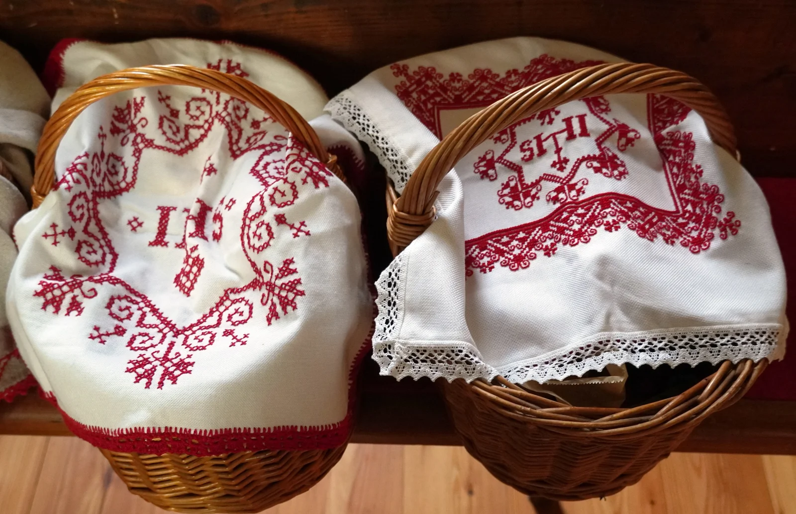 Woven Easter baskets lined with embroidered cloths containing ham, eggs, and bread arranged before church altar.