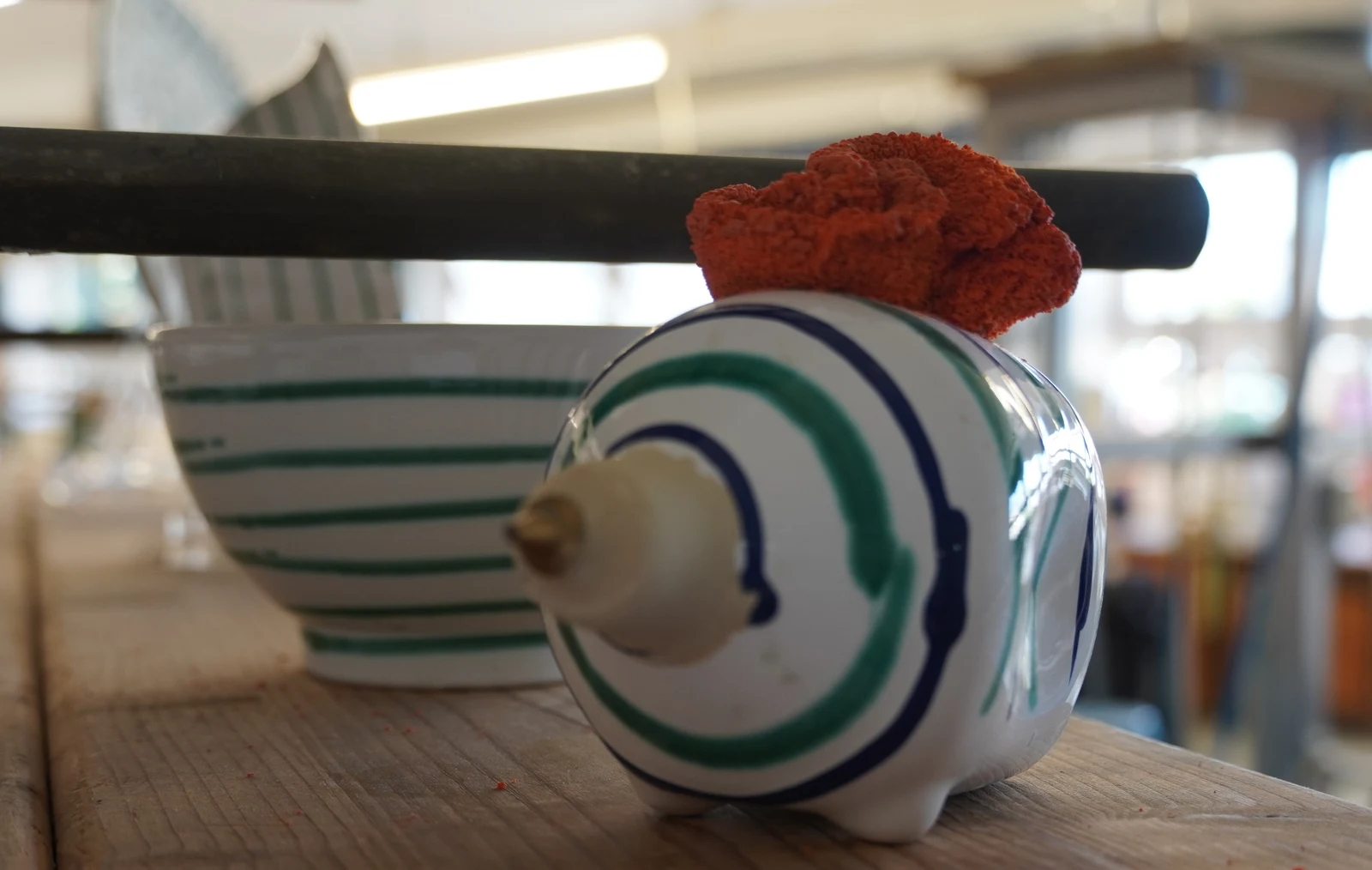 Traditional cow-horn painting vessel with fine nozzle and artisan sponge placed beside painted pottery.