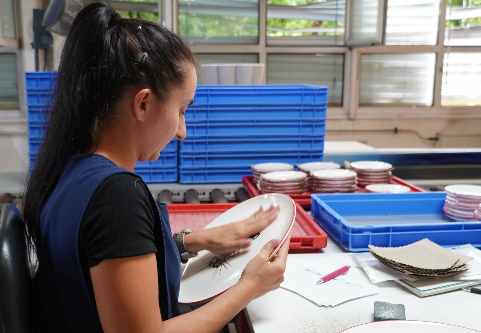 Pottery workshop in Upper Austria with artisan inspecting finished ceramic tableware on wooden drying shelves.