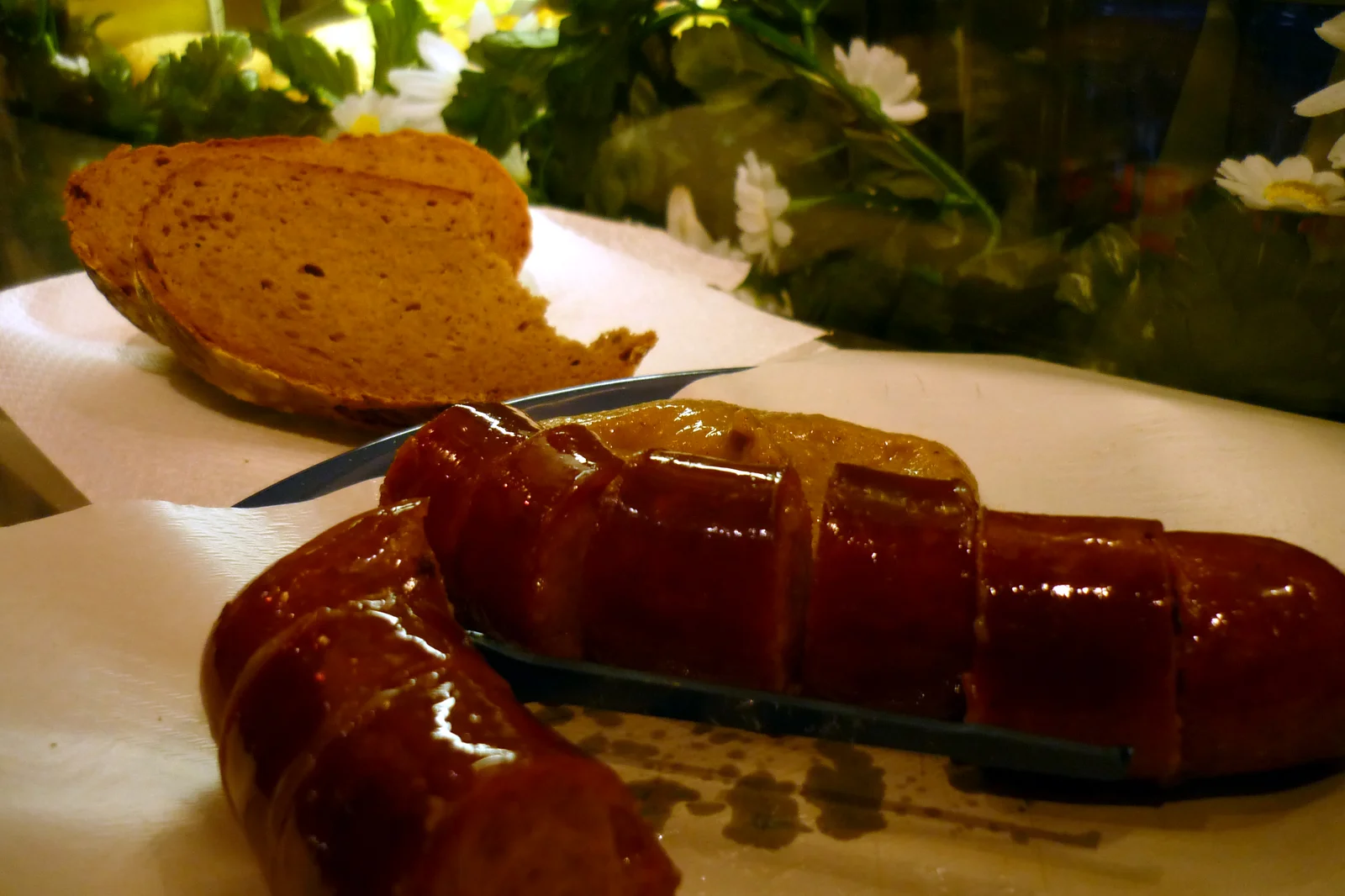 Sliced Käsekrainer sausage served with mustard and dark bread on a disposable plate.