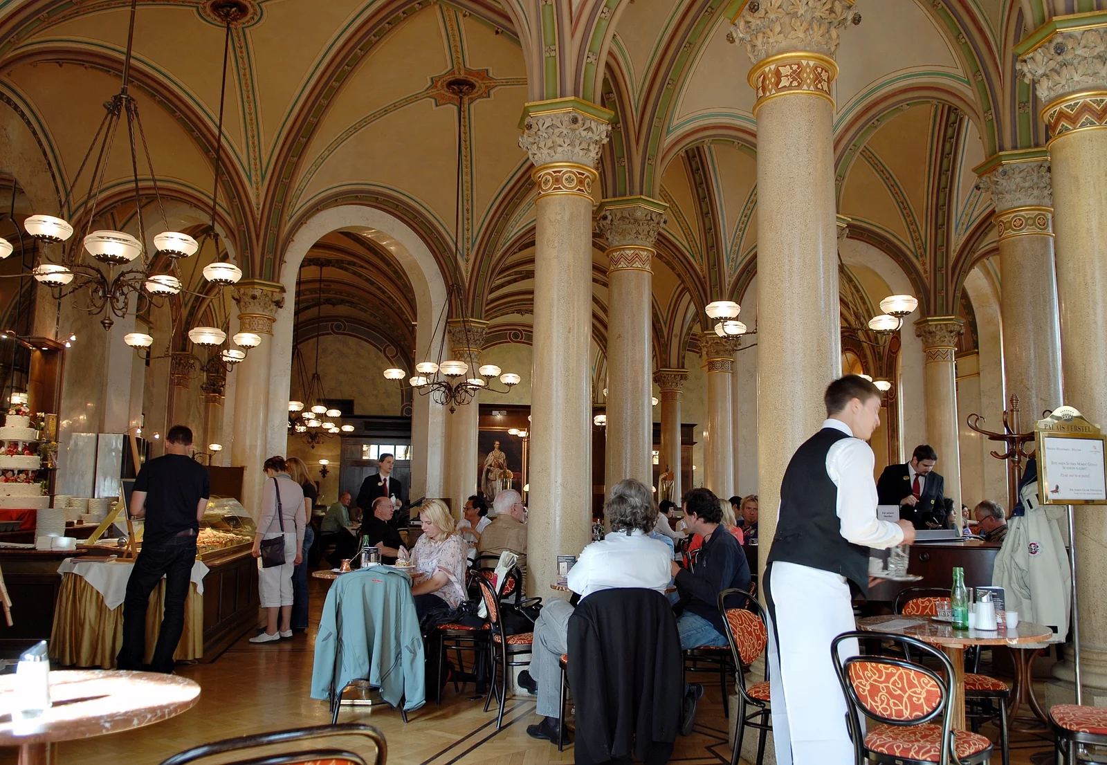 Neo-Renaissance vaulted dining hall of Café Central with patrons reading newspapers at marble tables.