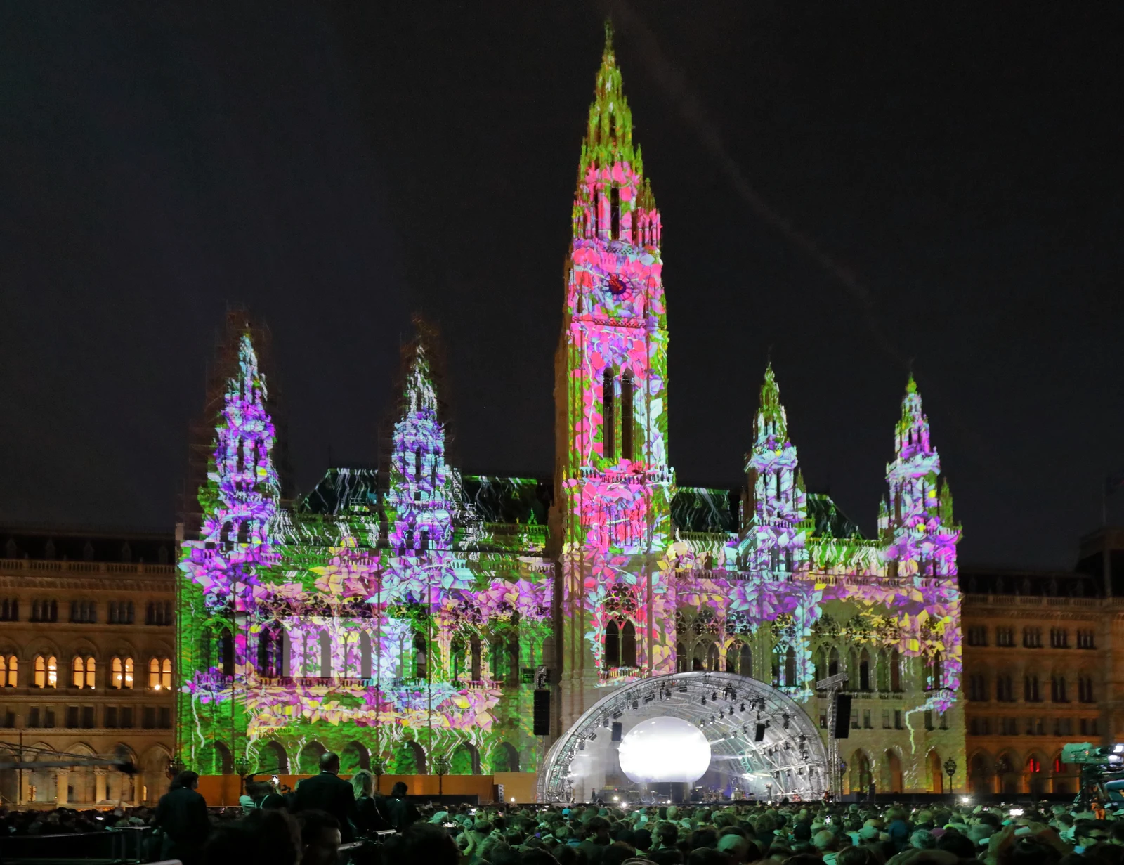 Spectacular illuminated outdoor stage in front of Vienna City Hall filled with festival audiences at night.