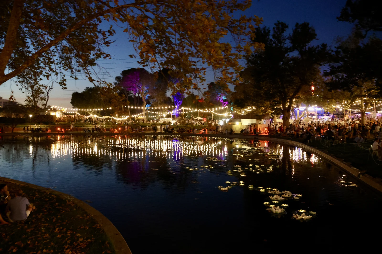 Open-air festival grounds featuring food stalls, timber seating, and performance tents in a public park.