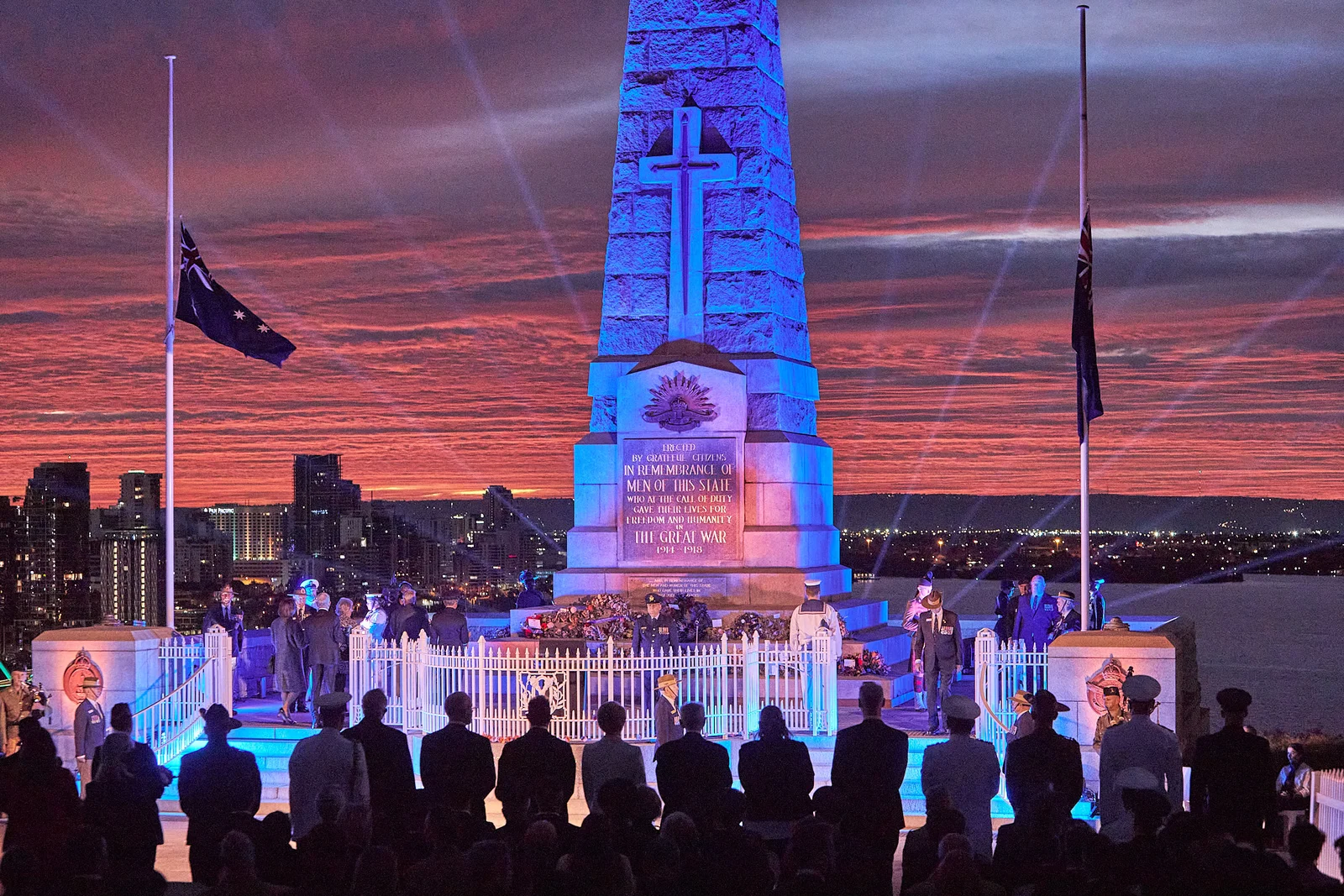 Solemn Anzac Day dawn service ceremony with memorial obelisk silhouetted against twilight sky.