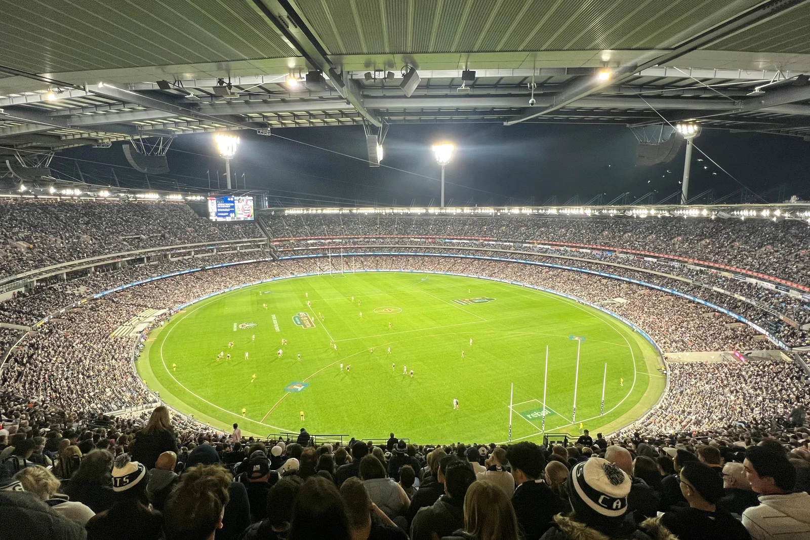 Wide view across the Melbourne Cricket Ground packed with cheering spectators watching an Australian Rules football game.