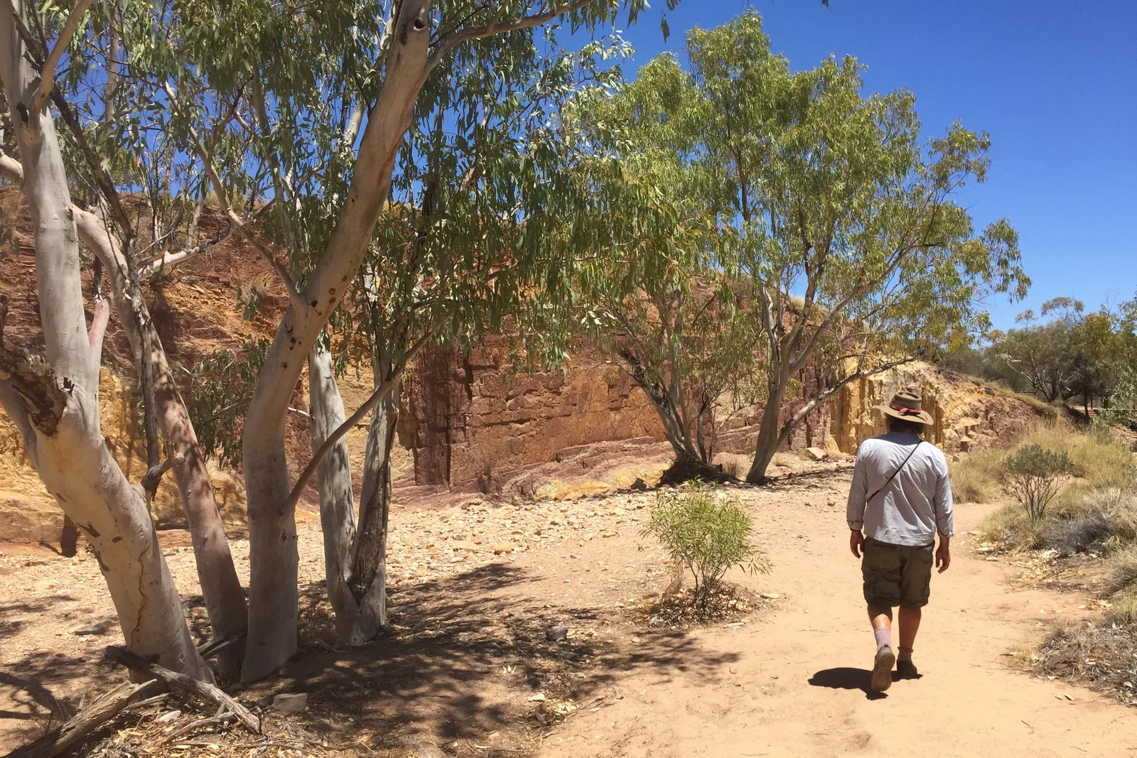 Banded cliffs of vibrant yellow, red, and white ochre rock in the Central Australian desert.