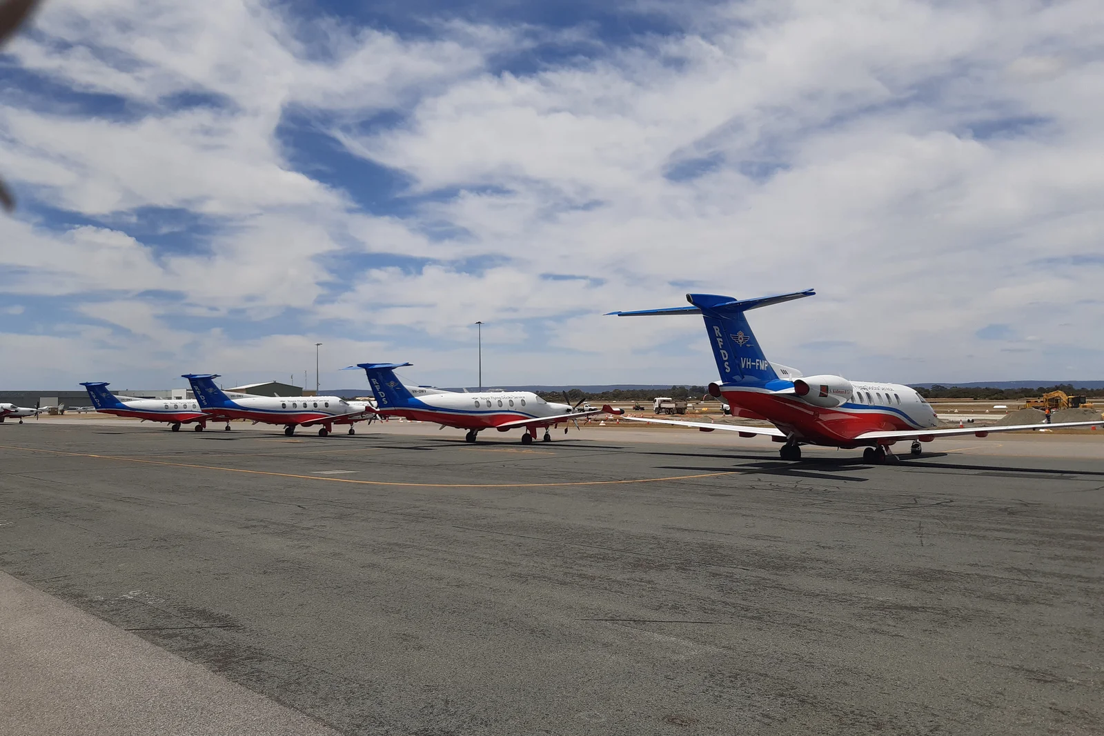 Lineup of RFDS turboprop air ambulance aircraft parked on tarmac outside an aviation hangar.