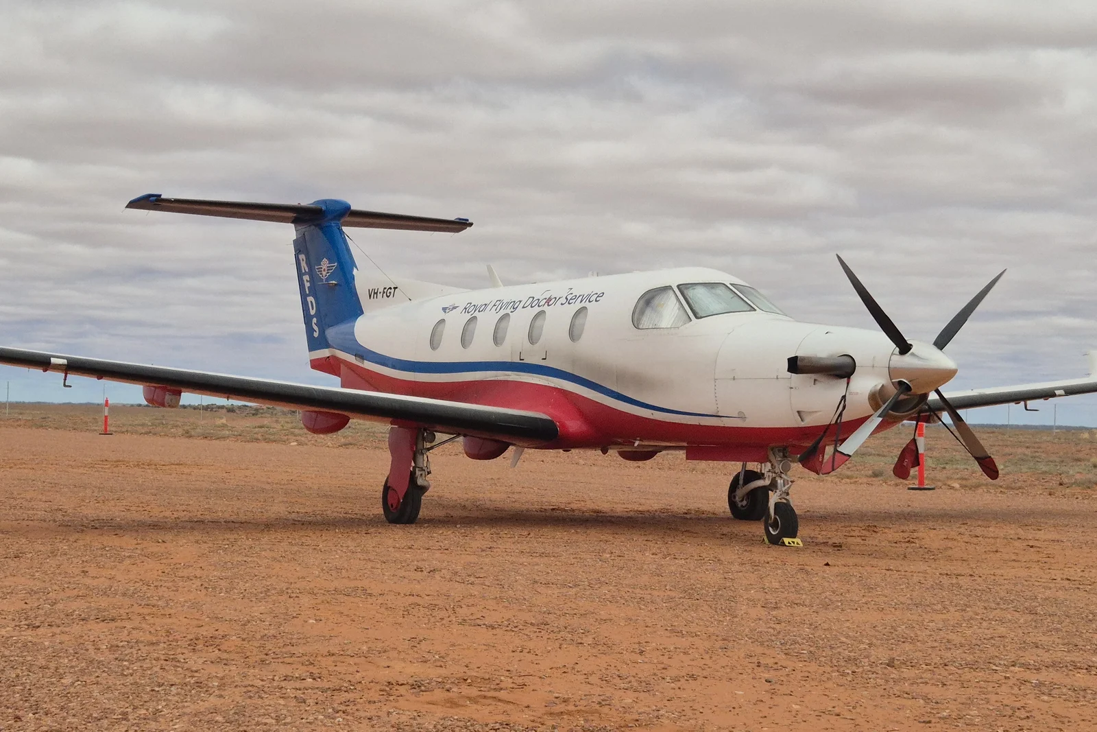 RFDS emergency medical aircraft parked on a red dirt outback runway under clear blue sky.