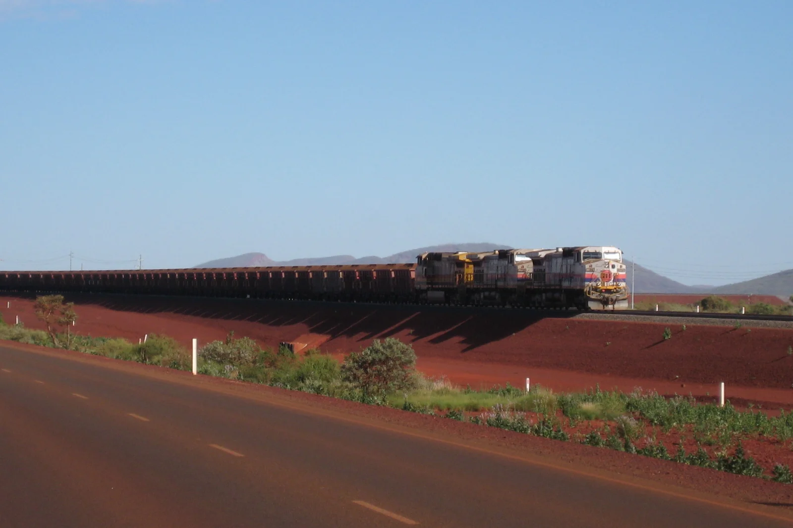 Long diesel-electric freight train hauling loaded iron ore wagons through the arid Pilbara desert.