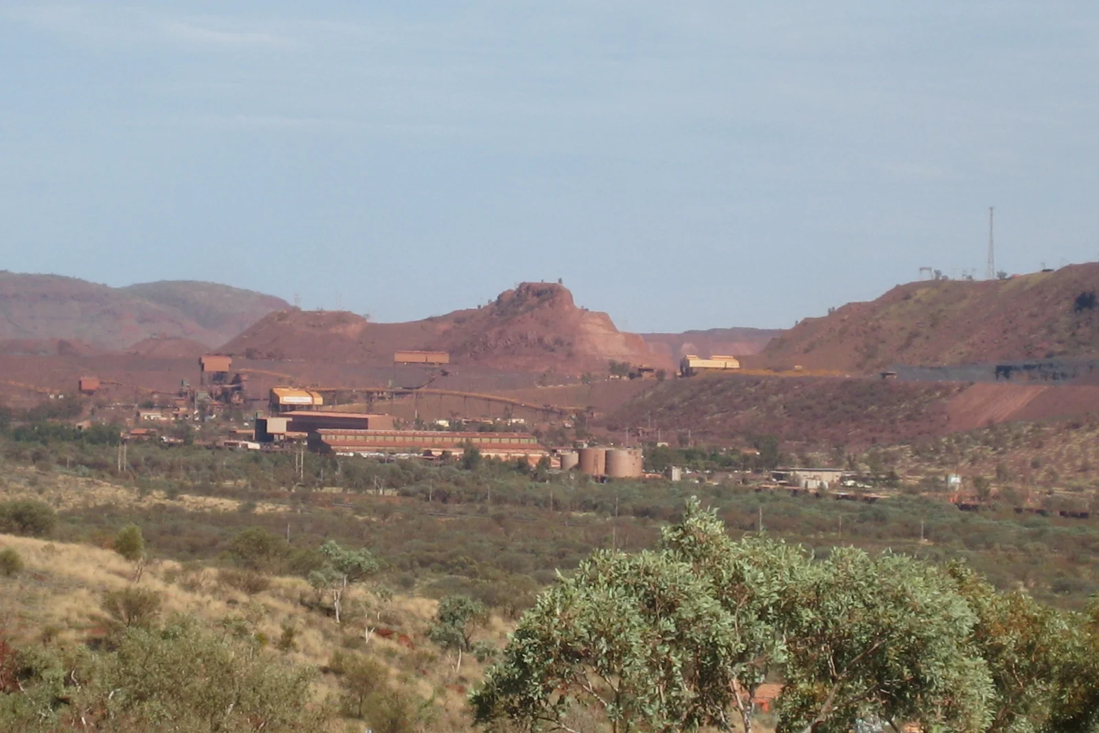 Expansive view of red open-pit mine terraces and industrial ore processing infrastructure.
