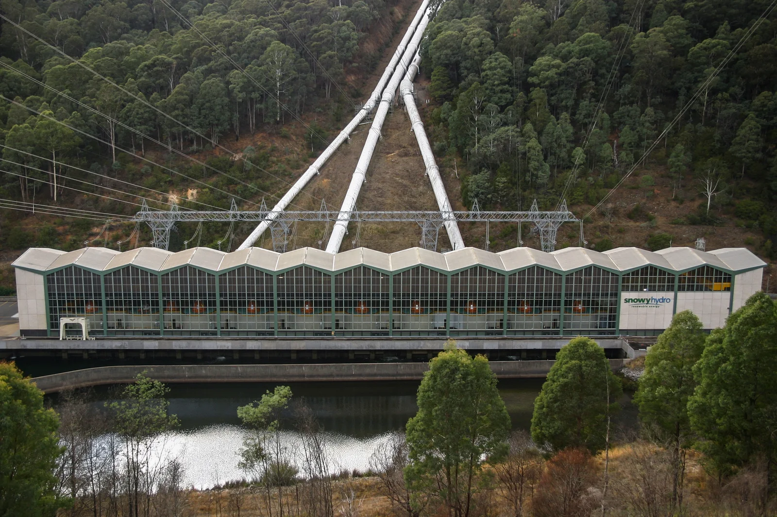 Hydroelectric power station at the base of an alpine mountain with steep penstock pipelines descending the hillside.