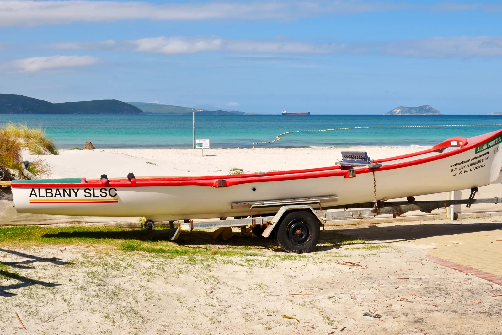 A classic Australian surf boat resting on the sandy beach facing the rolling ocean waves.
