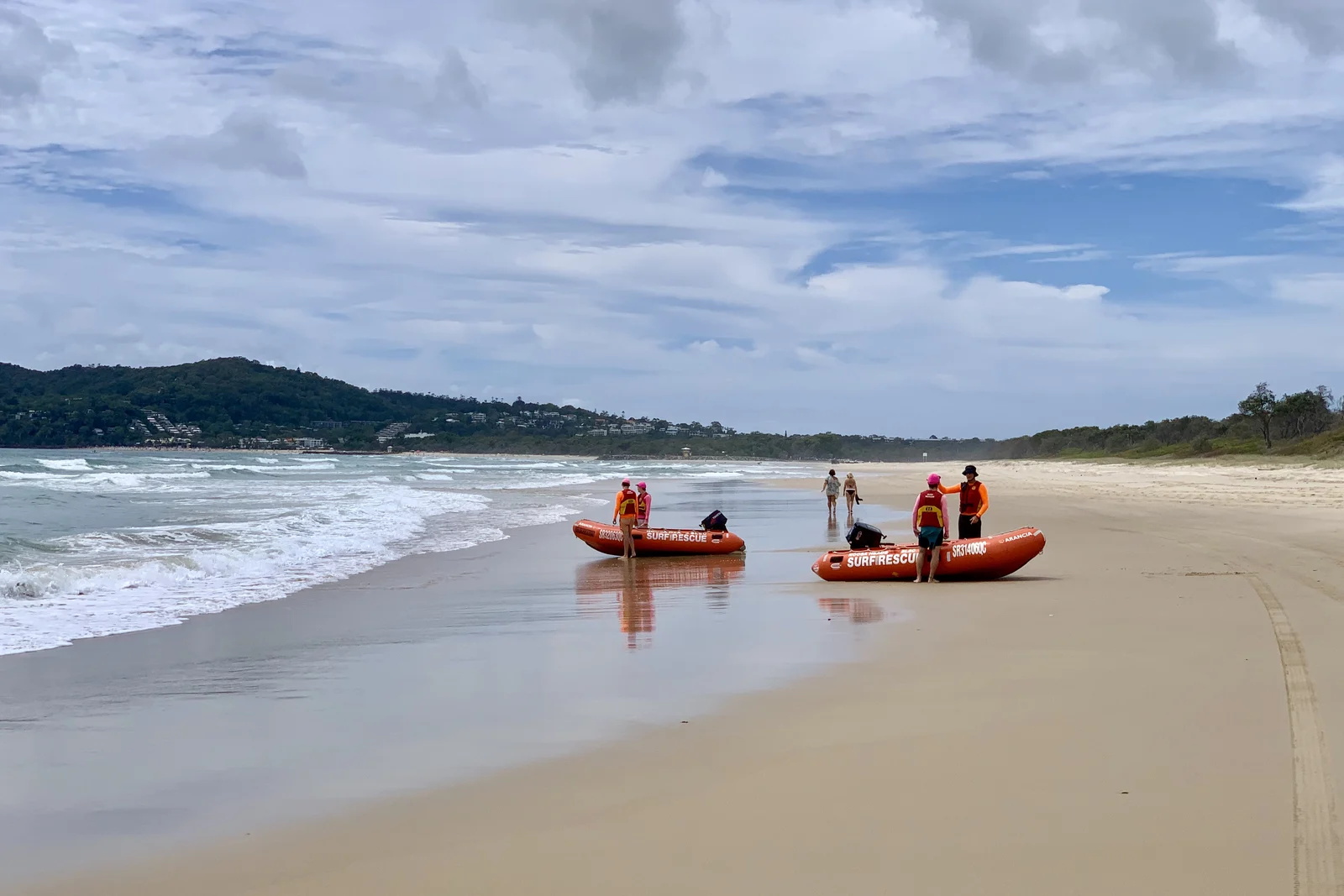 Volunteer surf lifesavers training on the sand with rescue equipment beside the ocean.