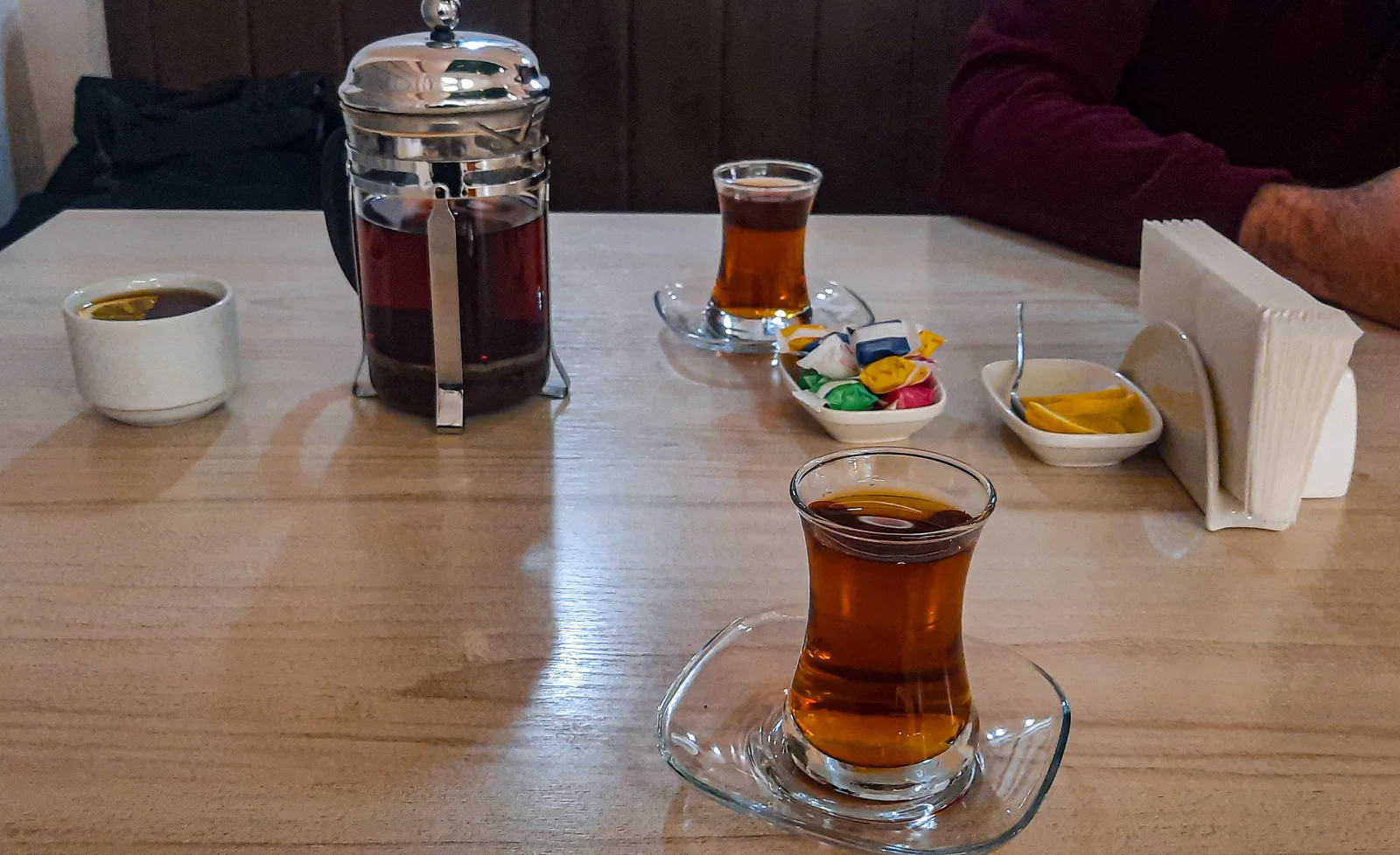 Pear-shaped armudu tea glass filled with amber black tea resting on a saucer with sliced fresh lemon and sugar cubes.