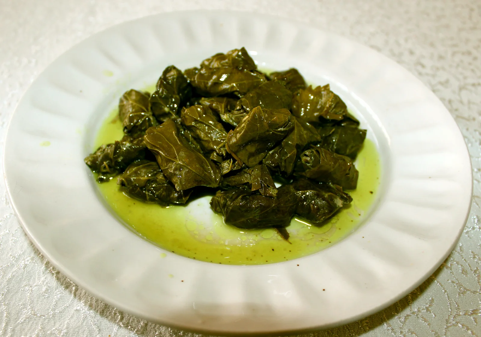Platter of small, tightly rolled green grapevine leaf dolma arranged in rows with a side bowl of garlic yogurt sauce.