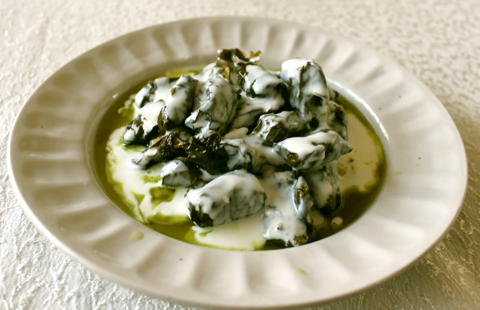 Top-down view of tender green stuffed grape leaves simmered to glistening tenderness in rich cooking broth.