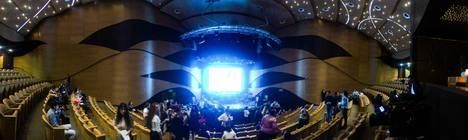 Spacious semi-circular auditorium with curved tiered seating facing a lit wooden stage.
