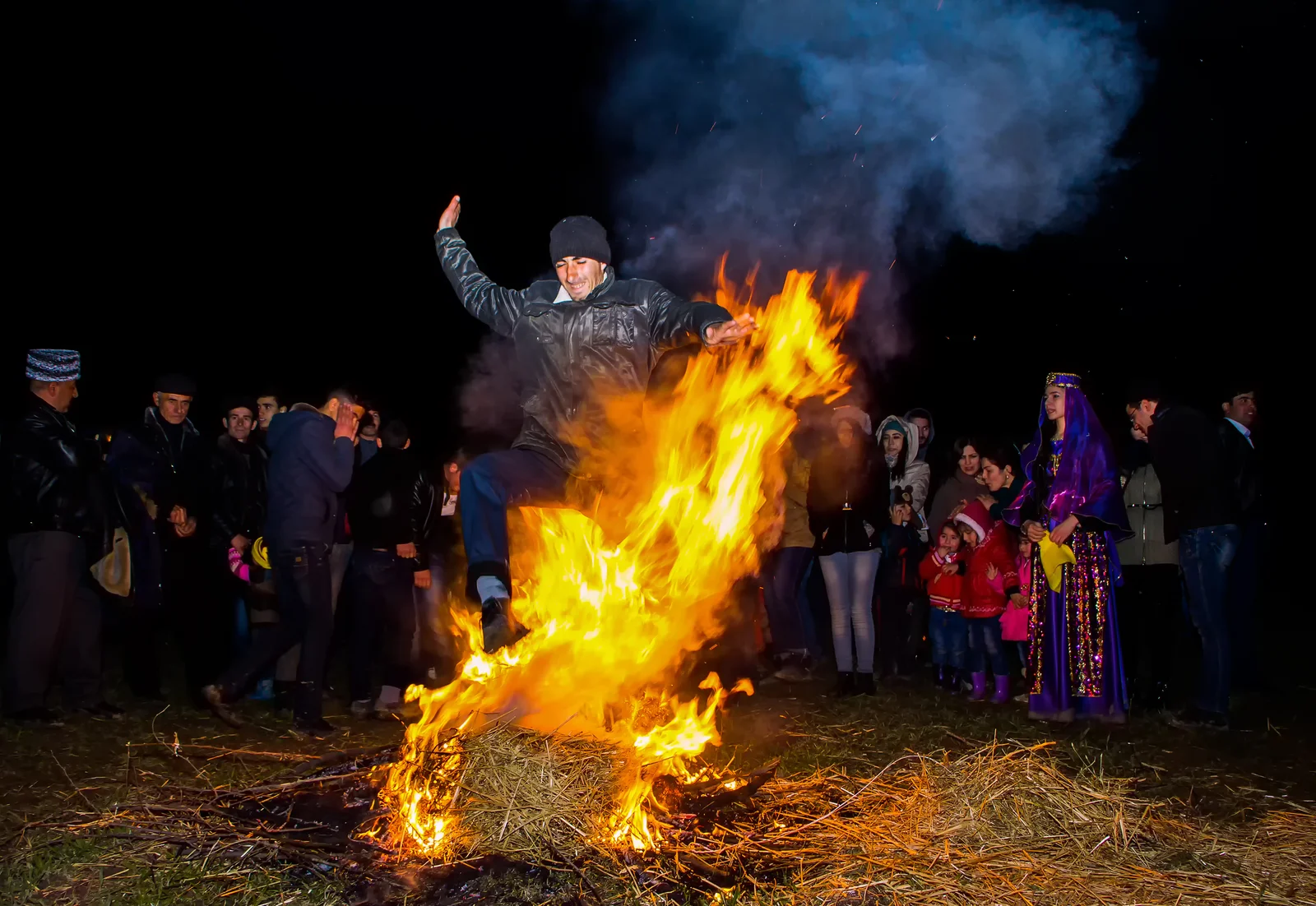 Bright orange flames of a traditional Novruz bonfire burning at dusk in an outdoor public space.