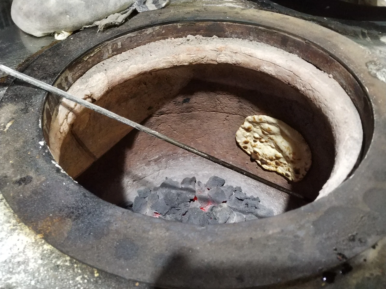 Top-down view into a glowing clay tandir oven showing round flatbreads clinging to the curving terracotta walls above glowing embers.