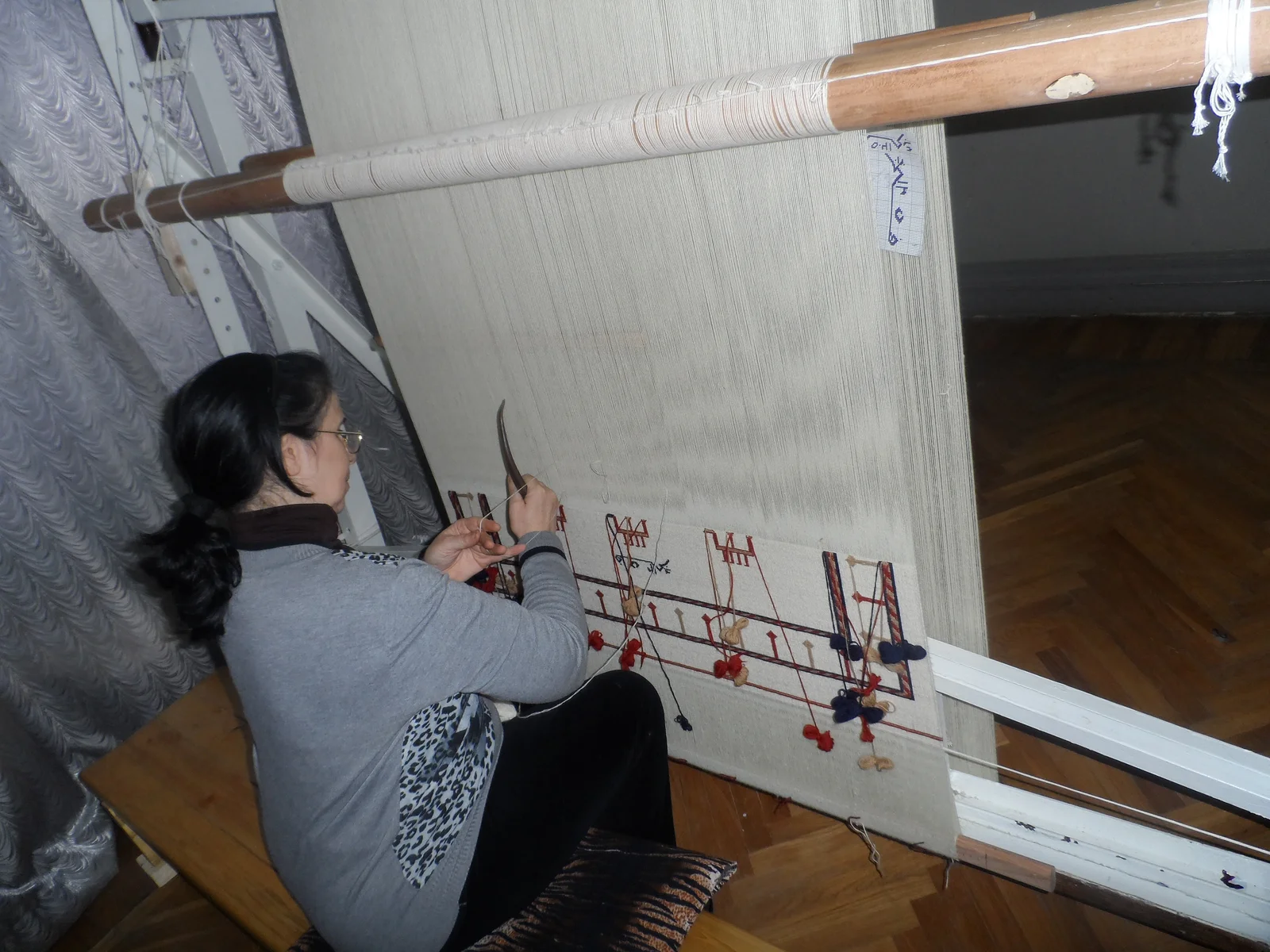 An artisan weaver hand-knotting colorful wool yarn onto a tall vertical carpet weaving loom.