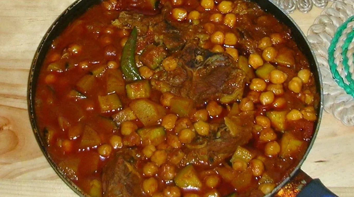 Tender pieces of meat and root vegetables simmering in a rich savory broth inside a deep metal cooking pot.