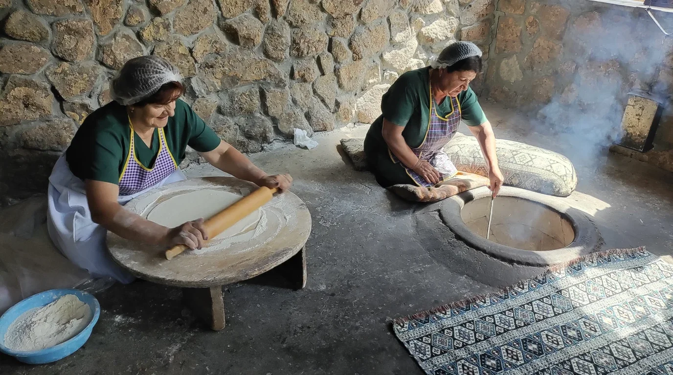 Bakery artisan stretching paper-thin sheets of phyllo dough with hands and a rolling pin over a flour-dusted table.