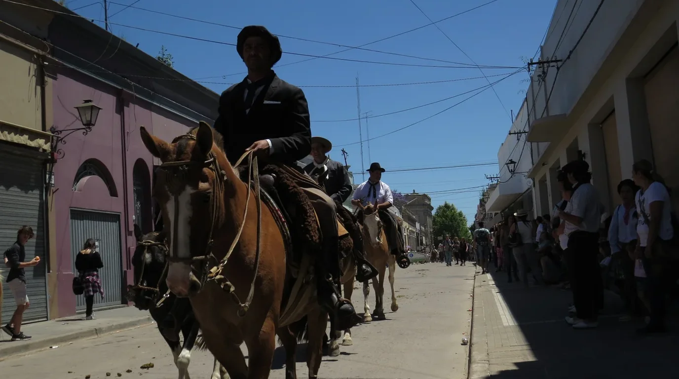 Traditional horse riders in festive attire parading across an open festival ground surrounded by spectators.