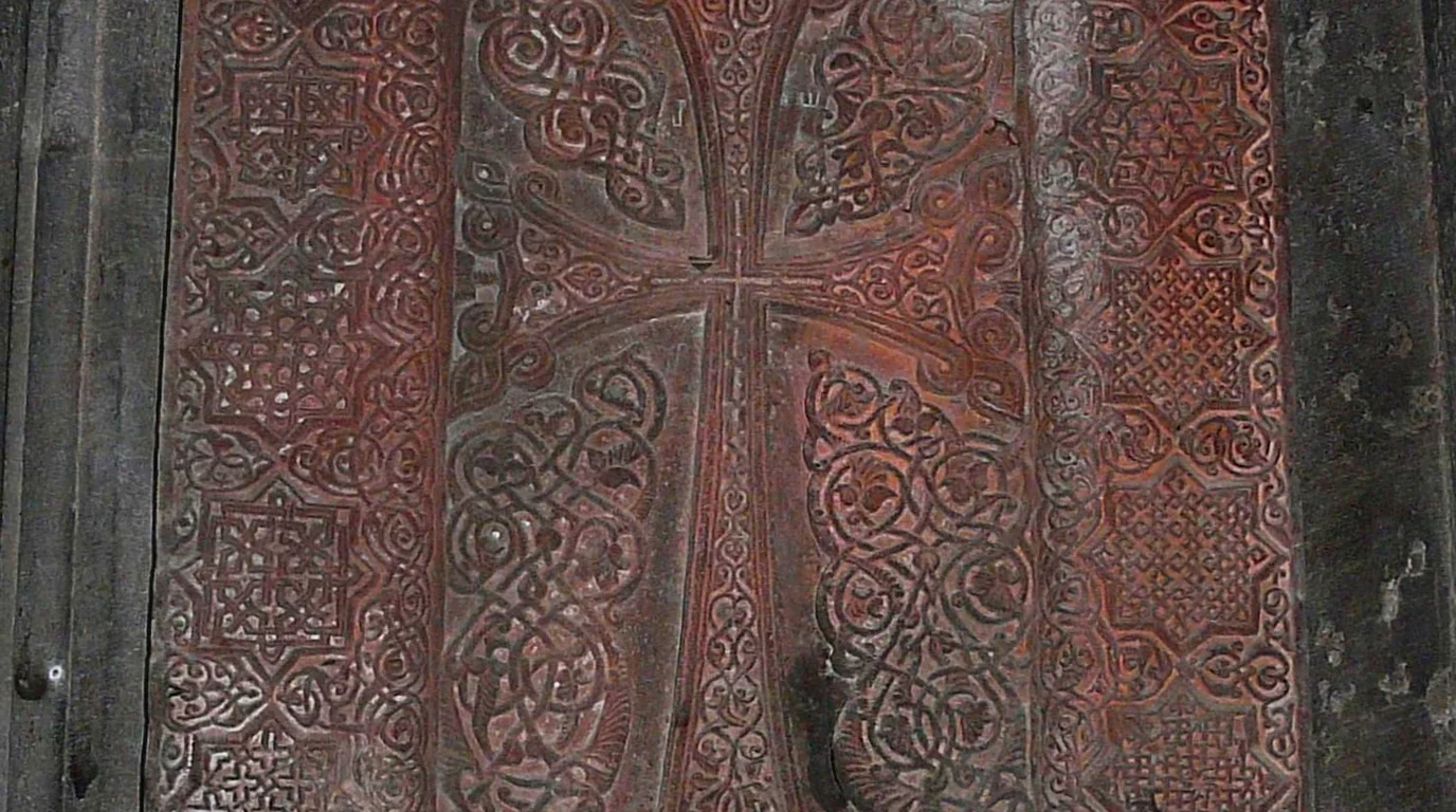 Close-up of weathered gray limestone surface showing intricate symbolic reliefs, geometric borders, and medieval heraldic emblems.