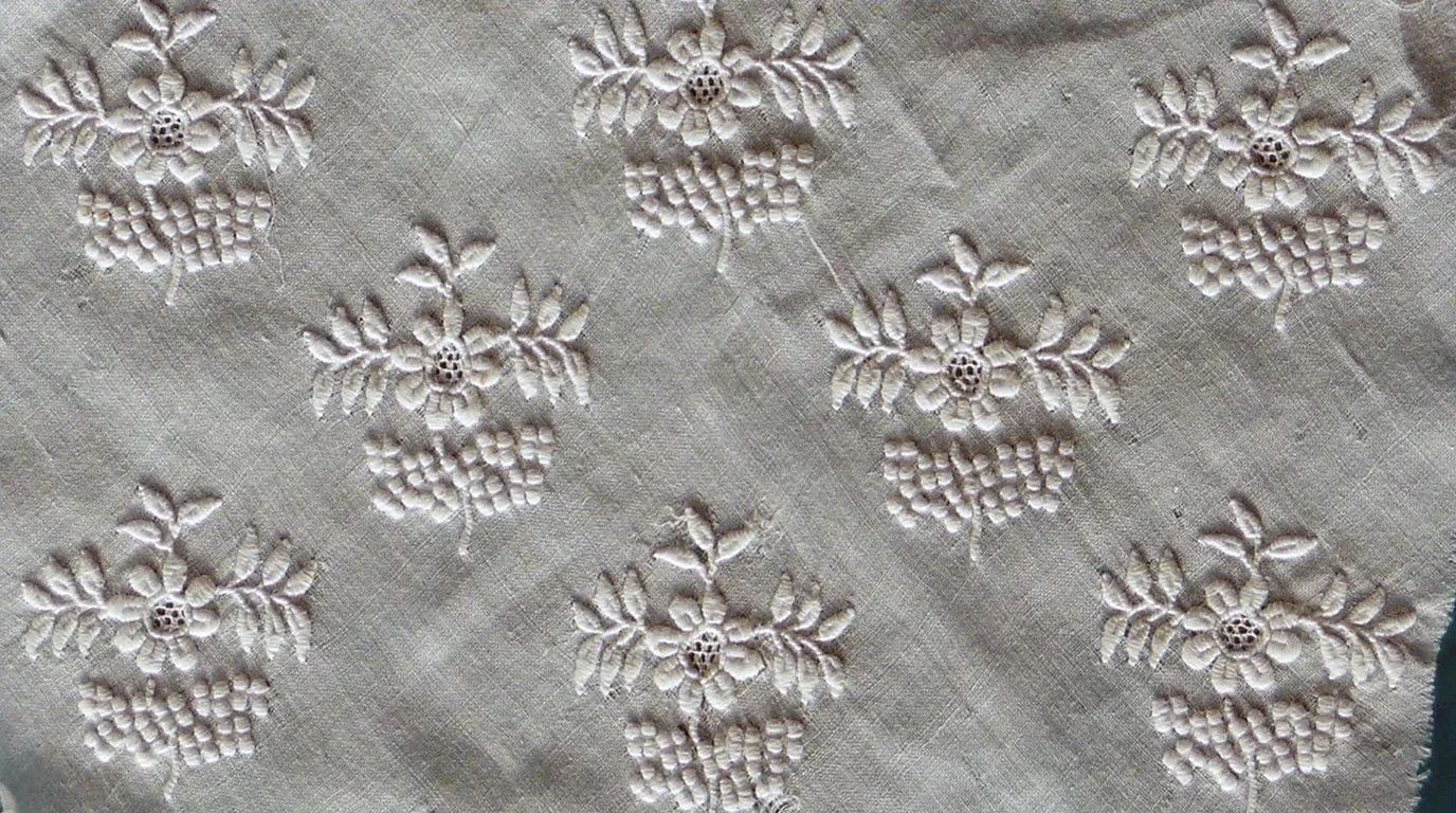 Detailed close-up of intricate dark indigo geometric cross-stitch needlework arranged in diamond patterns across handwoven linen fabric.