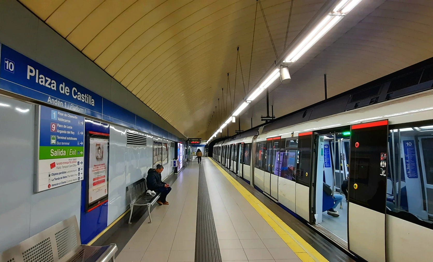 Platform 1 of Line 10 at Plaza de Castilla station showing a train with open doors and detailed multi-line transfer signs.