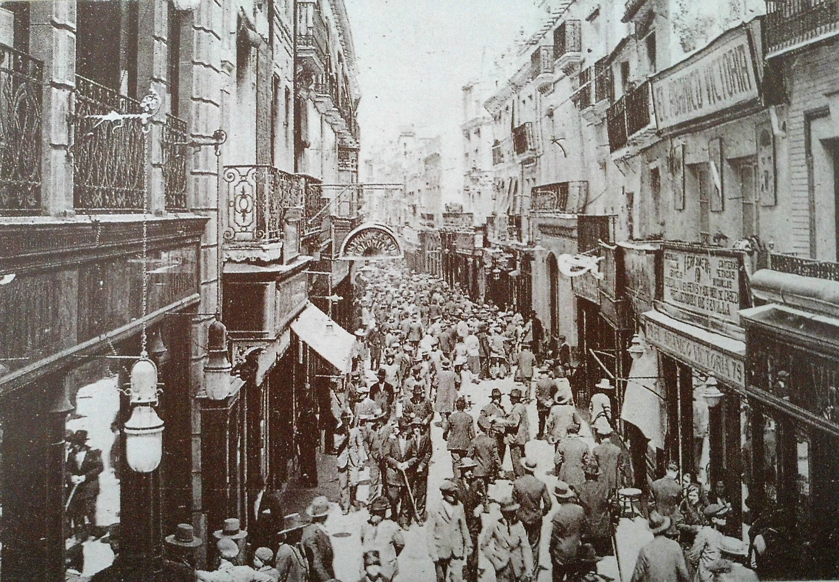 Pedestrians walking down shaded Calle Sierpes beneath suspended canvas toldos.