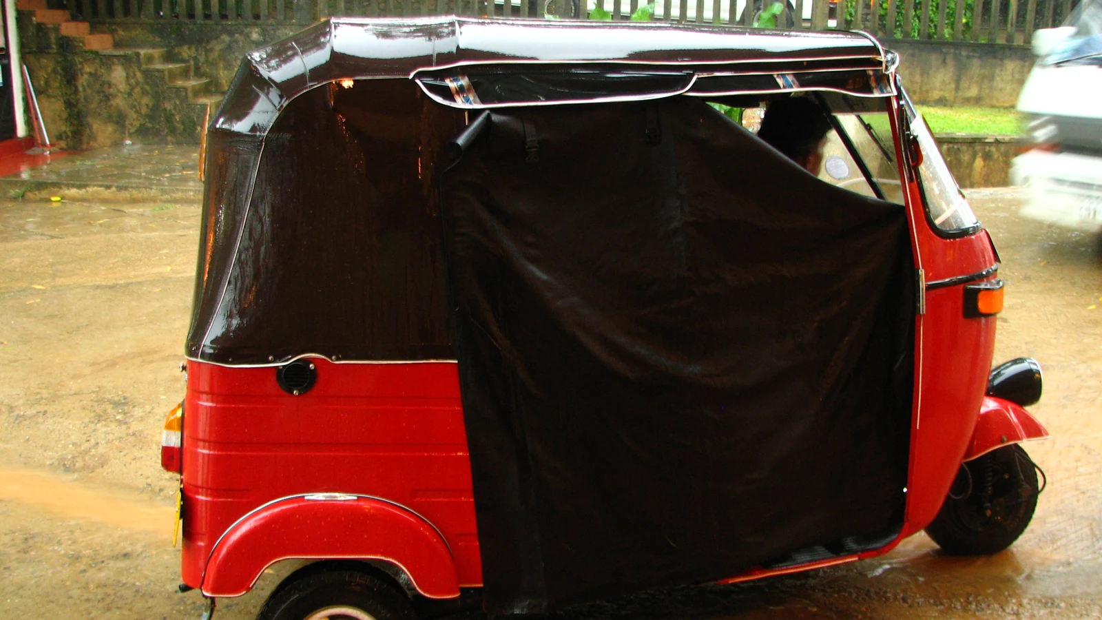 A three-wheeler taxi fitted with clear plastic side curtains to protect passengers from driving monsoon rain.