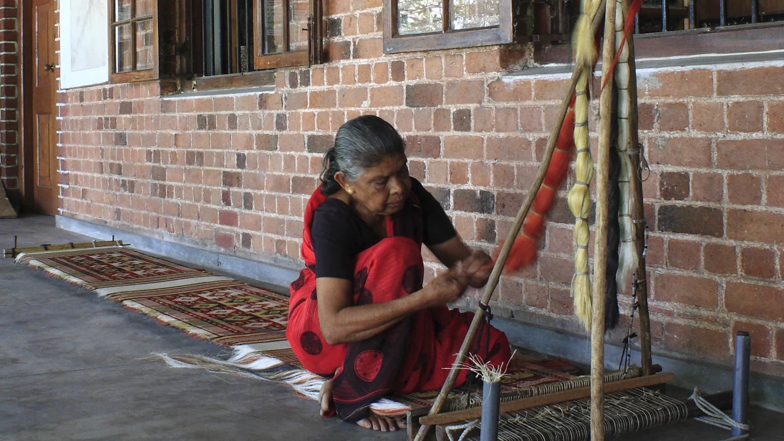 Close-up of a Dumbara weaving loom showing fiber strands inserted into the carved wooden wema stick.