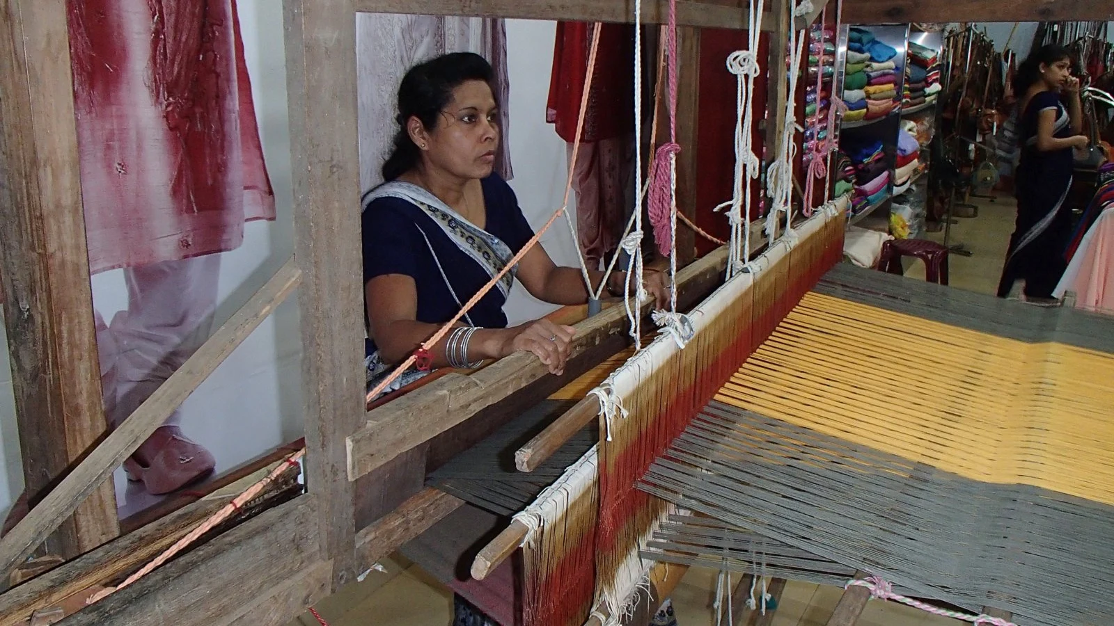 A master craftsman seated at a wooden weaving loom manipulating threads and shuttles in Sri Lanka.