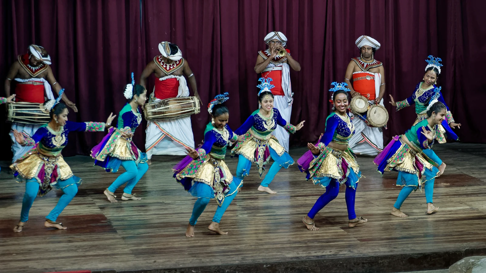Traditional Kandyan dancers in full sacred Ves costume and silver headdresses performing on stage.