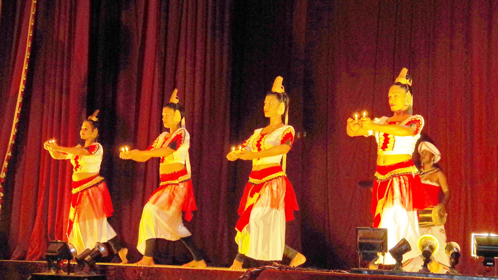 Dancers and drummers performing on the proscenium stage at the Kandyan Art Association auditorium.