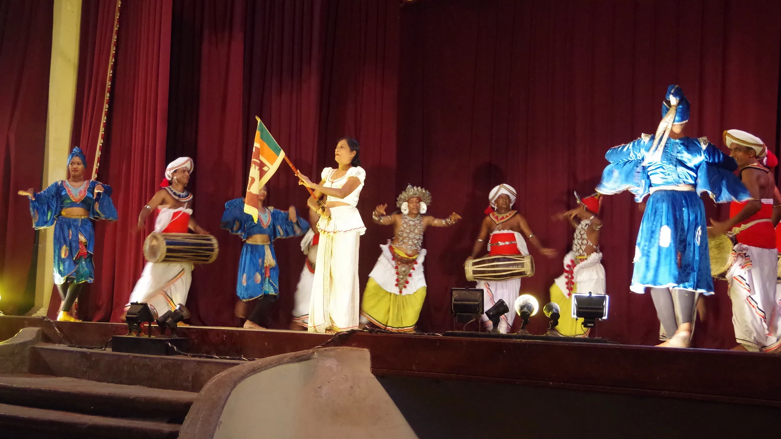 Ensemble of Kandyan dancers and Geta Beraya drummers framed under stage lights during a cultural recital.