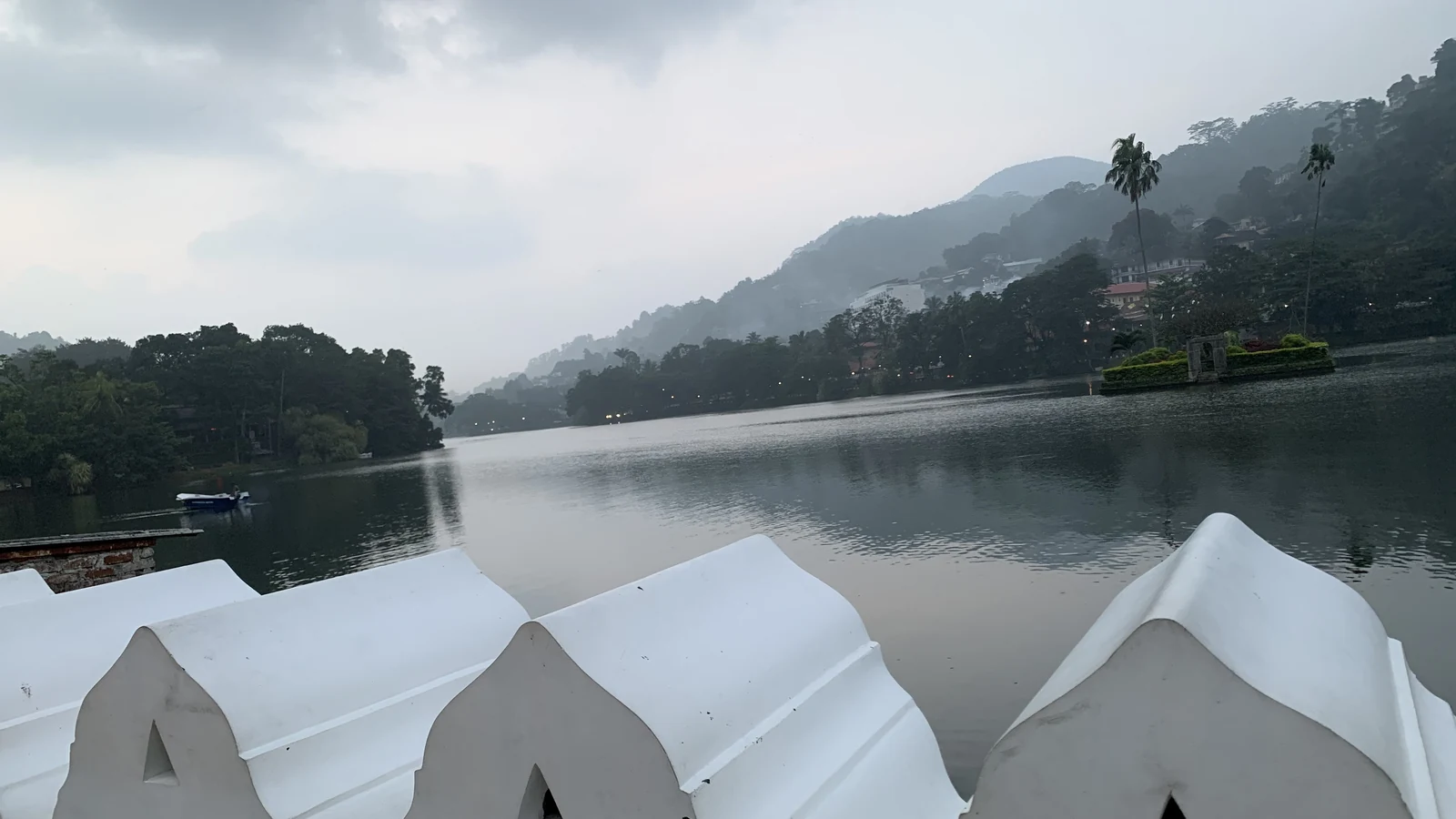 Morning mist over the tranquil waters of Kandy Lake reflecting hillside canopies.