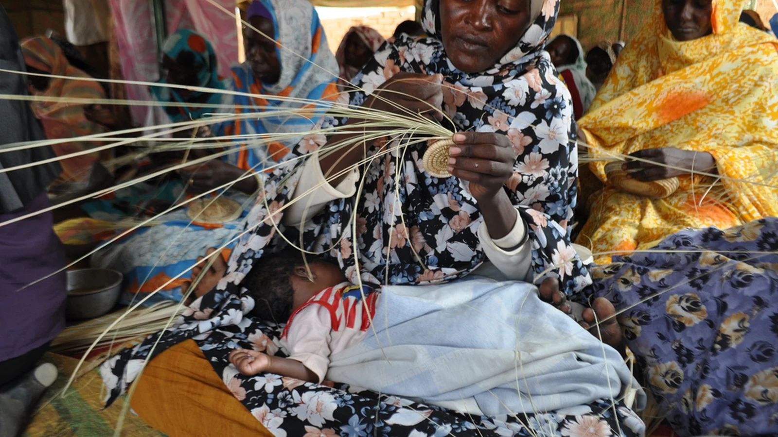 A Sudanese woman artisan coiling and stitching dyed palm fibers into a traditional basket.