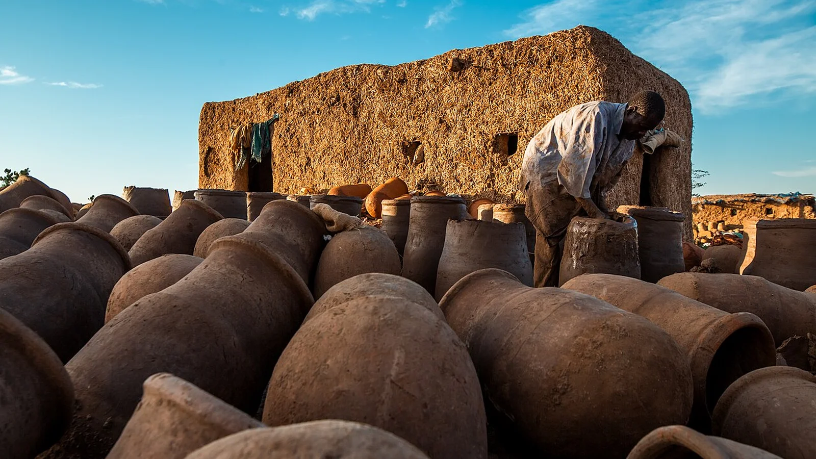 Rows of freshly shaped earthenware jars curing under the open sky outside an artisan pottery workshop.