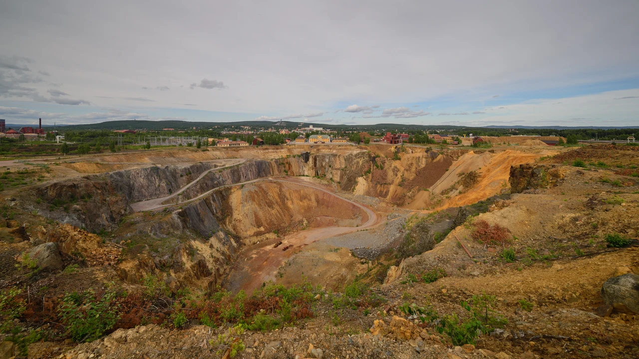 Panoramic landscape view across the historic Falun copper mine complex with red wooden headframes and spoil heaps.