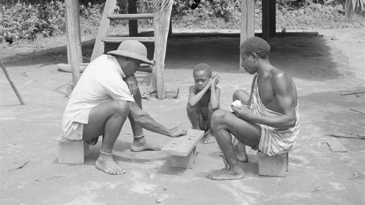 Villagers engaged in a game of Ba outside a traditional timber stilt dwelling in rural Suriname.