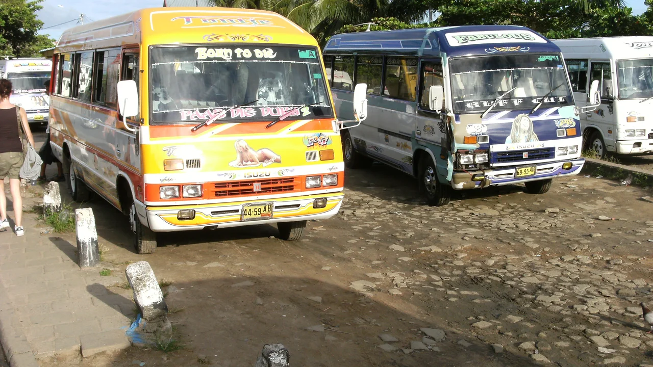A line of colorful privately operated passenger minibuses parked at a central transit station in downtown Paramaribo.