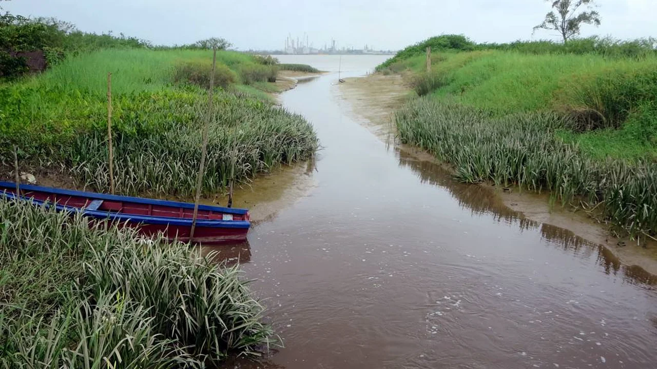 Open drainage canal cutting through coastal lowlands to convey heavy tropical rainwater away from settlements.